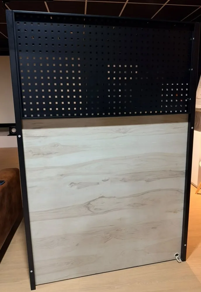 Free-standing partition: black steel pegboard on support poles above a laminate panel, in a showroom